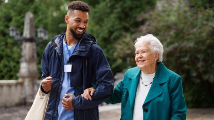 Pfleger begleitet Seniorin auf der Straße.