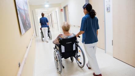 Zwei Pflegerinnen schieben ältere Patienten mit Rollstühlen durch einen Flur.