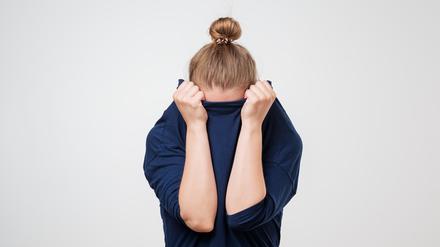 Eine Frau zieht sich beschämt ihren Pullover übers Gesicht.