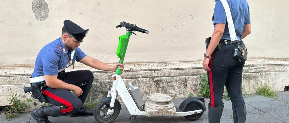 Zwei Carabinieri begutachten den Marmorsockel auf einem elektrischen Leihroller.