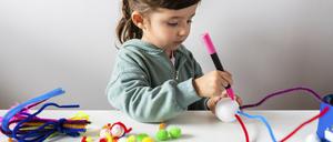 Ein Mädchen bastelt am Tisch ein Spielzeug aus Pfeifenreinigern und Styroporkugeln.