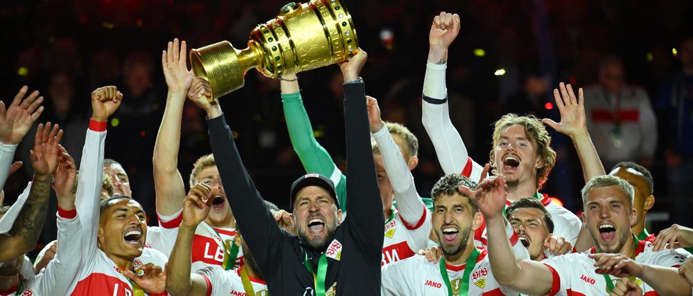 Der Trainer hält den Pokal in die Luft.