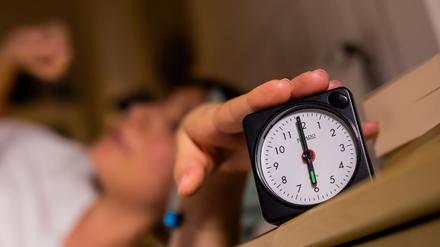 Eine Frau schaltet vom Bett aus einen auf sechs Uhr gestellten Wecker aus.
