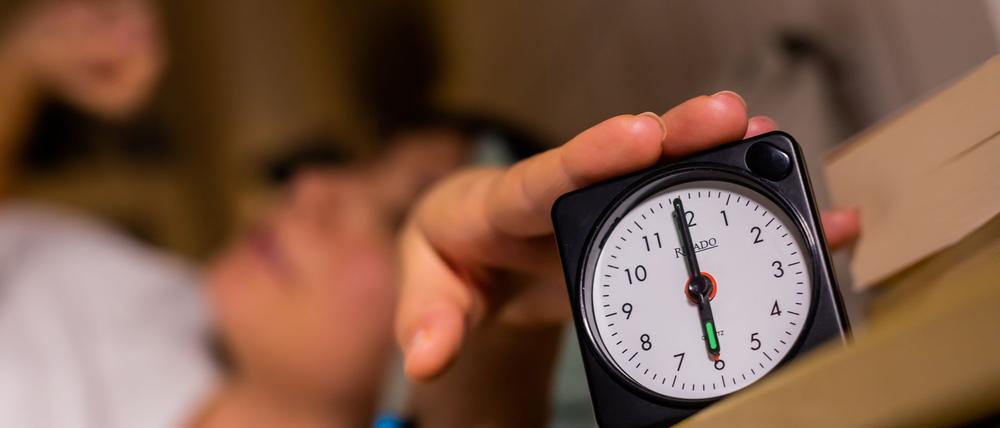 Eine Frau schaltet vom Bett aus einen auf sechs Uhr gestellten Wecker aus.