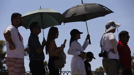 Las Vegas: Menschen tragen Regenschirme, um sich vor der Sonne zu schützen, während sie darauf warten, ein Foto am „Welcome to Las Vegas“-Schild zu machen.