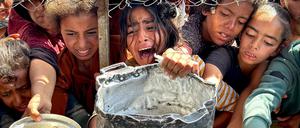 Palästinensische Kinder versuchen im Gebiet Al-Mawasi im Gazastreifen, mit ihren Töpfen Nahrungsmittel zu bekommen, die von Wohltätigkeitsorganisationen verteilt werden.
