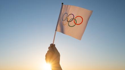  Eine Hand mit der Olympischen Fahne im Gegenlicht.