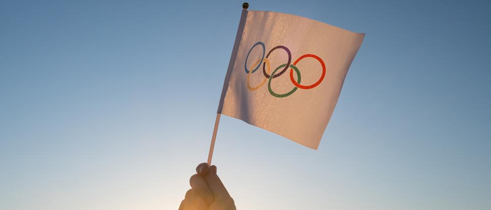 Eine Hand mit der Olympischen Fahne im Gegenlicht.