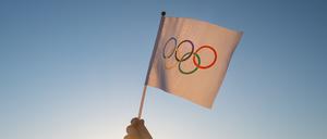  Eine Hand mit der Olympischen Fahne im Gegenlicht.