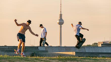 Männer skaten auf dem Tempelhofer Feld in Berlin, im Hintergrund ist der Fernsehturm zu sehen.