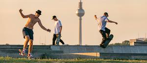 Männer skaten auf dem Tempelhofer Feld in Berlin, im Hintergrund ist der Fernsehturm zu sehen.