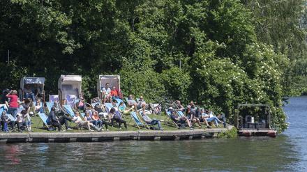 Zahlreiche Menschen sitzen am Vatertag im Treptower Park am Ufer auf der Insel der Jugend.