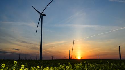 Der Sonnenaufgang leuchtet über der Landschaft mit Windenergieanlagen und einem Kran auf einer Baustelle für ein neues Windrad. 