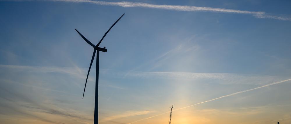 Der Sonnenaufgang leuchtet über der Landschaft mit Windenergieanlagen und einem Kran auf einer Baustelle für ein neues Windrad.