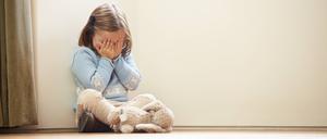 Ein Mädchen sitzt auf dem Boden und hält ihr Gesicht mit ihren Händen zu.