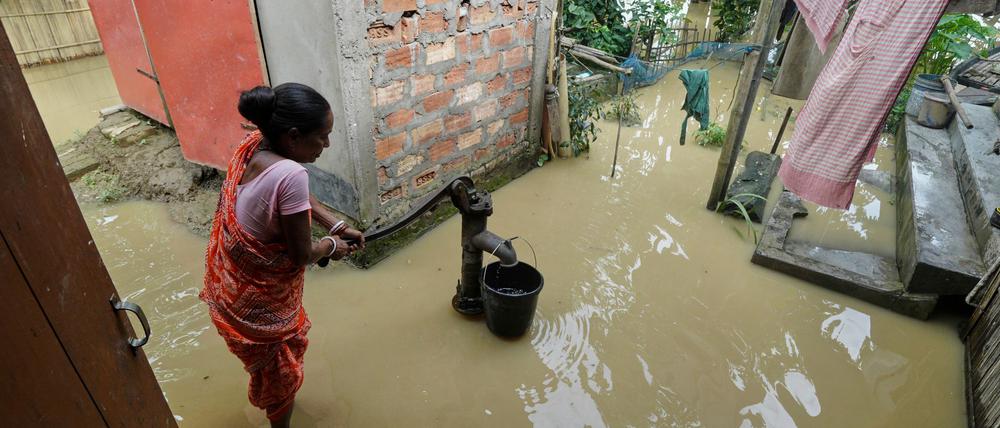 Eine Frau versucht in der überfluteten Umgebung ihres Hauses, Wasser zu sammeln.