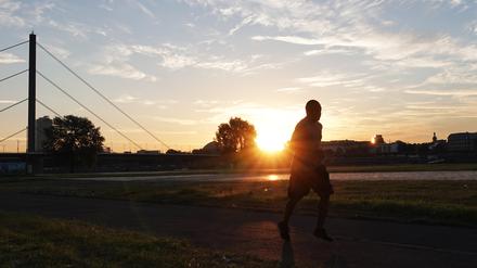 in Jogger bei Sonnenaufgang am Rheinufer in Düsseldorf. 