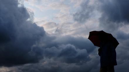 Ein Mann geht mit einem Regenschirm vor aufziehenden dunklen Wolken spazieren. 