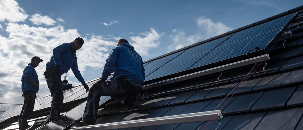 Mitarbeiter einer Firma montieren Photovoltaikmodule auf dem Dach eines Wohnhauses.