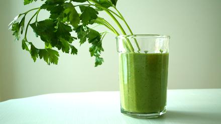 Ein grüner Smoothie in einem transparenten Glas ist mit einem Büschel zur Seite hängender Petersilie garniert. (Symbolbild)