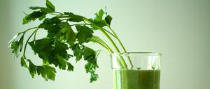 Ein grüner Smoothie in einem transparenten Glas ist mit einem Büschel zur Seite hängender Petersilie garniert. (Symbolbild)