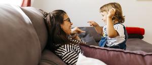Eine Mutter sitzt mit ihrer Tochter auf einem Sofa, in ein spielerisches Gespräch vertieft.