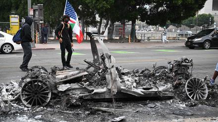 People look at the charred remains of a burned Waymo vehicle in the street following a night of protests in response to federal immigration operations in Los Angeles, on June 9, 2025. Los Angeles was on edge Monday after violent clashes between demonstrators and security forces over immigration raids, with the Californian governor vowing to sue President Donald Trump for deploying National Guard soldiers. Police stood watch after ordering people not to gather in the city's downtown where cars were torched over the weekend and security forces fired tear gas at protesters. Protests in Los Angeles, home to a large Latino population, broke out on June 6, triggered by immigration raids that resulted in dozens of arrests of what authorities say are illegal migrants and gang members. (Photo by RONALDO SCHEMIDT / AFP)