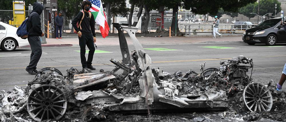 People look at the charred remains of a burned Waymo vehicle in the street following a night of protests in response to federal immigration operations in Los Angeles, on June 9, 2025. Los Angeles was on edge Monday after violent clashes between demonstrators and security forces over immigration raids, with the Californian governor vowing to sue President Donald Trump for deploying National Guard soldiers. Police stood watch after ordering people not to gather in the city's downtown where cars were torched over the weekend and security forces fired tear gas at protesters. Protests in Los Angeles, home to a large Latino population, broke out on June 6, triggered by immigration raids that resulted in dozens of arrests of what authorities say are illegal migrants and gang members. (Photo by RONALDO SCHEMIDT / AFP)