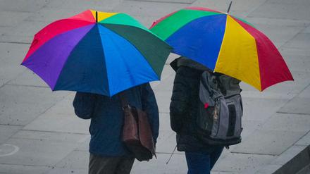 Zwei Passanten mit bunten Regenschirmen gehen bei leichtem Regen durch die Potsdamer Innenstadt.