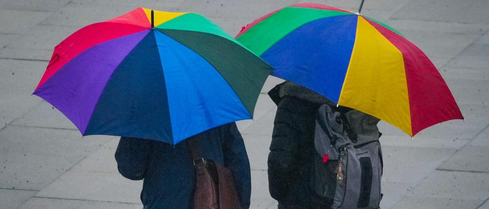 Zwei Passanten mit bunten Regenschirmen gehen bei leichtem Regen durch die Potsdamer Innenstadt.
