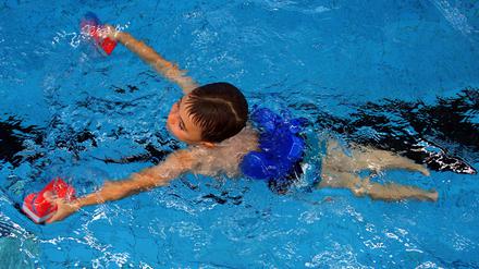Schwimmkurs: ein Sechsjähriger ist mit Schwimmhilfen im Becken unterwegs.