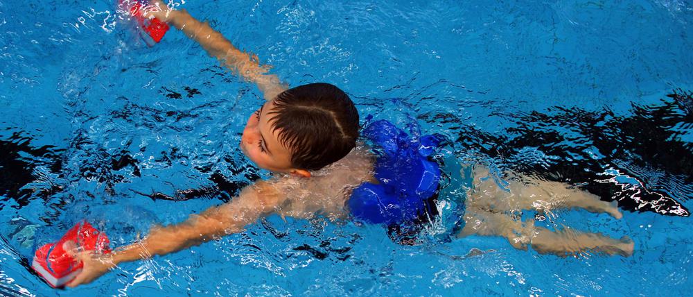 Schwimmkurs: ein Sechsjähriger ist mit Schwimmhilfen im Becken unterwegs.