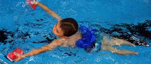 Schwimmkurs: ein Sechsjähriger ist mit Schwimmhilfen im Becken unterwegs.