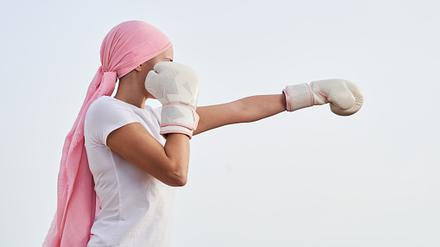 Unrecognizable female cancer patient with pink headscarf, placed in punching position with boxing gloves in her hands as a sign of combat. Concept of fighting and beating cancer.
