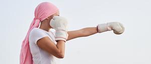 Unrecognizable female cancer patient with pink headscarf, placed in punching position with boxing gloves in her hands as a sign of combat. Concept of fighting and beating cancer.