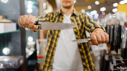 Ein junger Mann in einem Messerladen hält zwei Messer, um sie zu vergleichen.