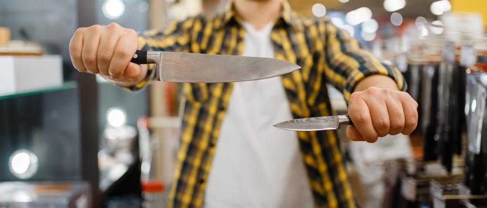 Ein junger Mann in einem Messerladen hält zwei Messer, um sie zu vergleichen.