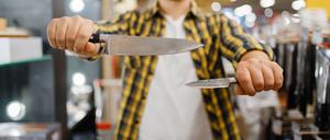 Ein junger Mann in einem Messerladen hält zwei Messer, um sie zu vergleichen.
