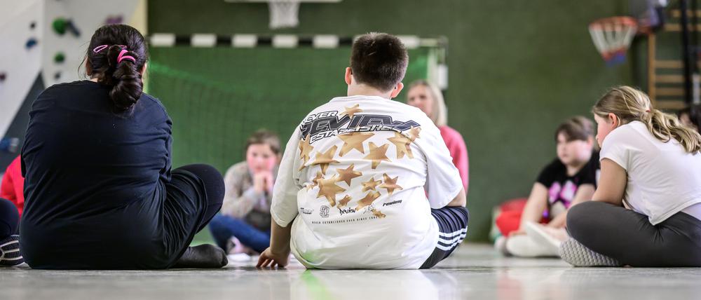 Teilnehmer einer Trainingsgruppe für übergewichtige Kinder sitzen in einer Sporthalle.