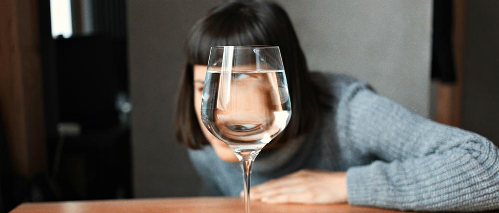 Eine Frau schaut durch ein Wasserglas.