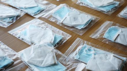 Tüten mit FFP2-Masken und OP-Masken liegen auf einem Tisch.