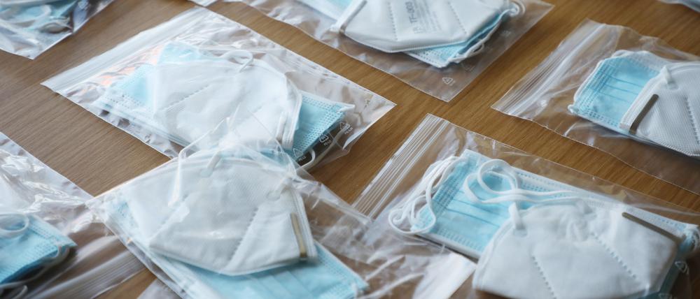 Tüten mit FFP2-Masken und OP-Masken liegen auf einem Tisch.