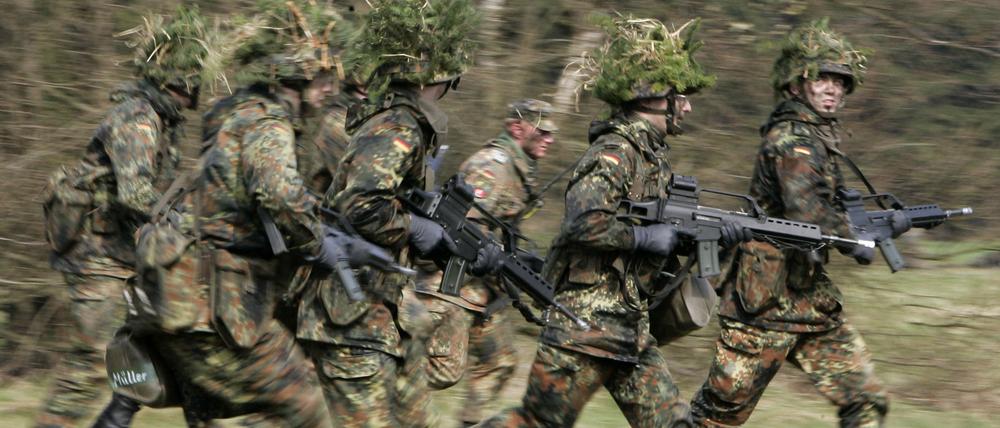 Mit Blattwerk und Gras getarnte Wehrpflichtige von den Panzergrenadieren rennen mit ihren Waffen im Rahmen ihrer Grundausbildung bei einer Übung über das freie Gelände der Knüll Kaserne in Schwarzenborn (Archivfoto).