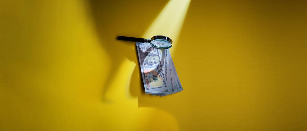 Eine Lupe über einem Bündel mit Dollarscheinen (Illustration).