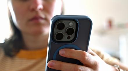 Ein jugendliches Mädchen sitzt mit ihrem Smartphone auf dem Sofa und schaut auf das Display.