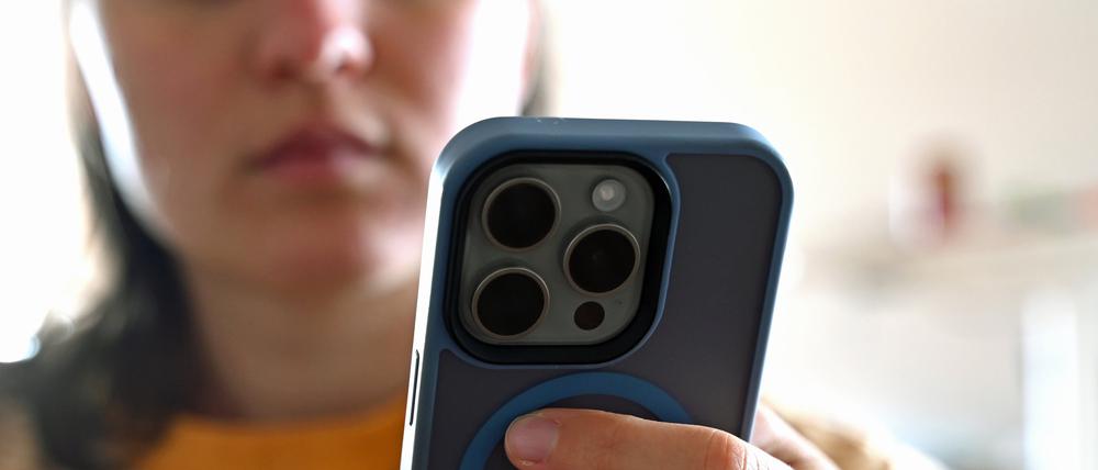 Ein jugendliches Mädchen sitzt mit ihrem Smartphone auf dem Sofa und schaut auf das Display.