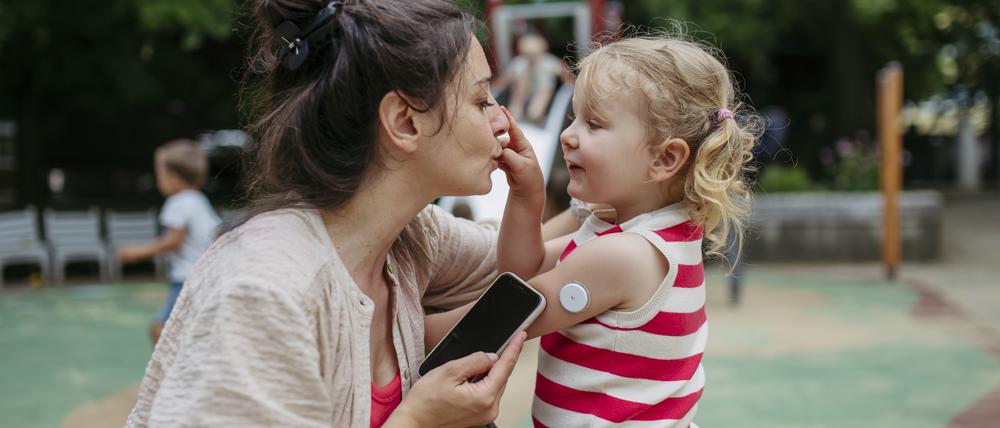 Mit neuen Geräten können Diabetes-Patienten kontinuierlich den Blutzucker prüfen. Hier eine Mutter, die bei ihrer Tochter die Daten des Blutzuckermessgerätes auf der Schulter untersucht.