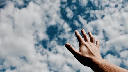 Eine Hand streckt sich Richtung Himmel.