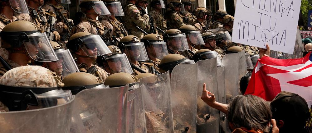 U.S. Marines stand guard as a person displays a sign reading „Fuck the Migra (referring to the U.S. Immigration and Customs Enforcement)„ during protest against U.S. President Donald Trump’s policies and federal immigration sweeps during a No Kings Day demonstration in Los Angeles, California, U.S., June 14, 2025.  REUTERS/David Ryder 