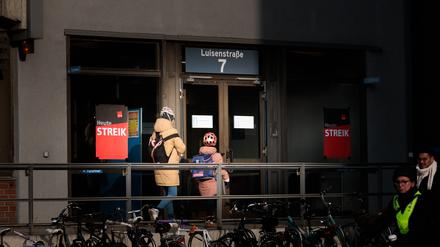 Menschen gehen an einem Streik-Schild am Eingang ins Charité-Gebäude vorbei, während sich Beschäftigte der Charité Facility Management (CFM) zu einem unbefristeten Streik vor dem Charité-Gebäude versammeln.
